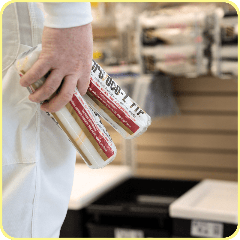close up of painting contractor holding paint rollers in a paint store and infront of a wall of painting tools and accessories